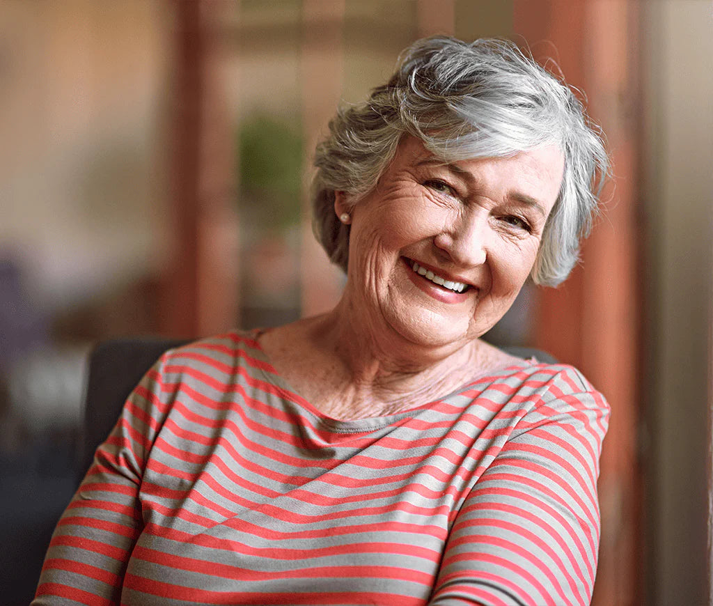 Smiling elderly woman in a striped shirt sitting indoors.