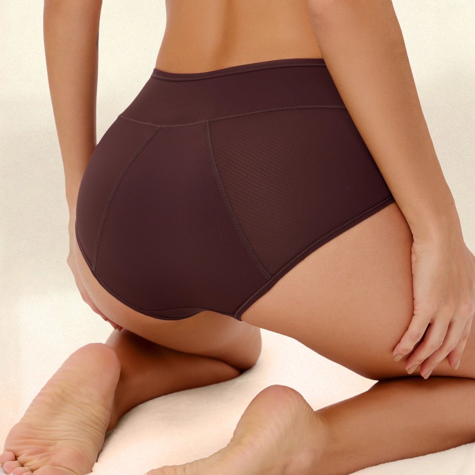 Person wearing brown high-waisted underwear, kneeling on a light surface.