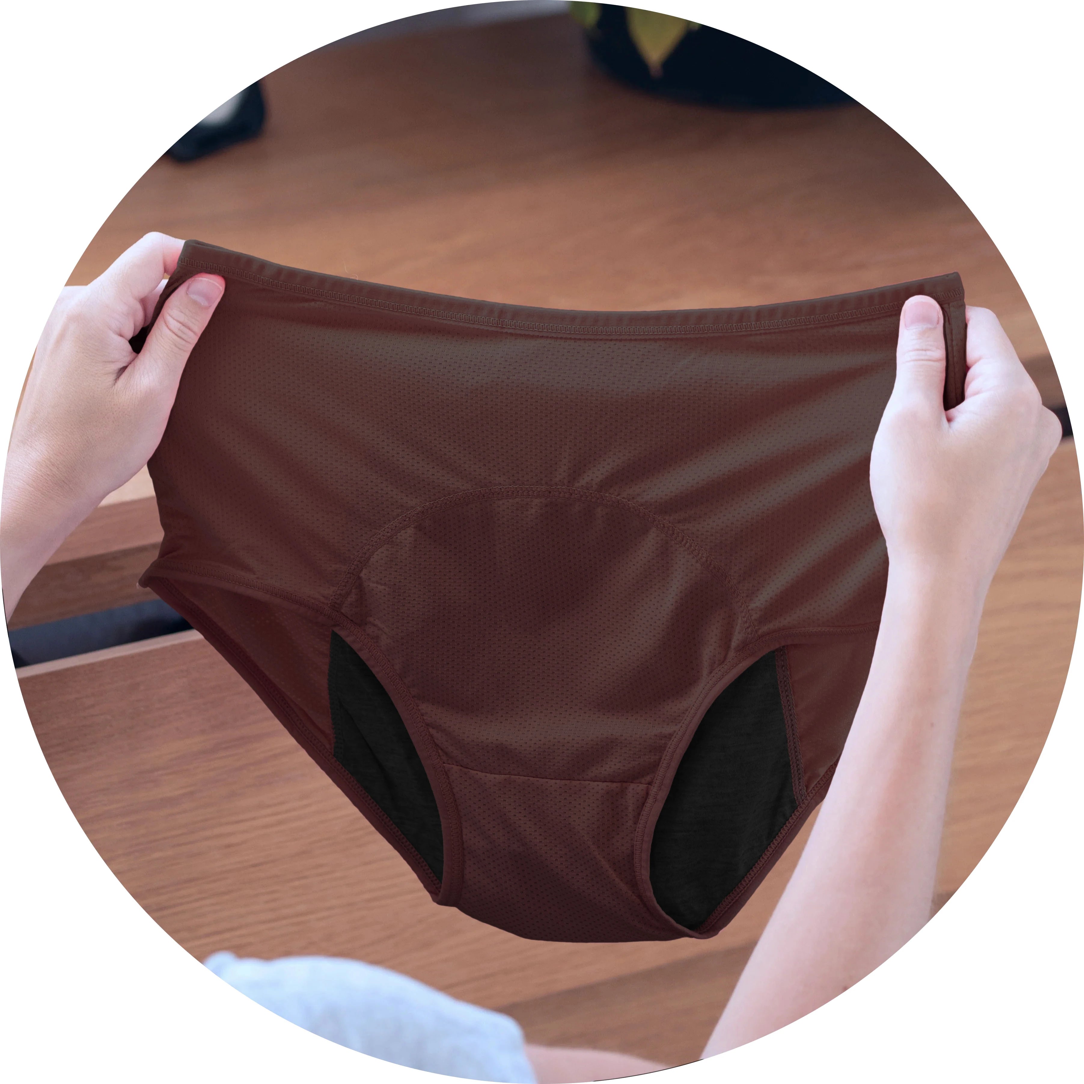 Hands holding a pair of brown underwear above a wooden surface.